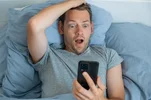 handsome-impressed-man-reading-news-smartphone-shocked-expression-bed-morning-guy-amazed-rece...webp