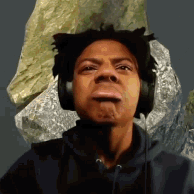a man wearing headphones making a funny face with a rock in the background