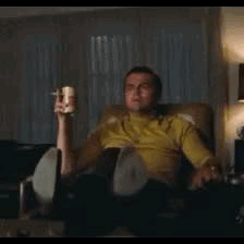 a man is sitting in a chair holding a bottle of beer and a cup of coffee .