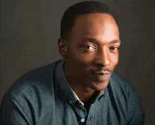 a man in a blue shirt is looking at the camera with a serious look on his face