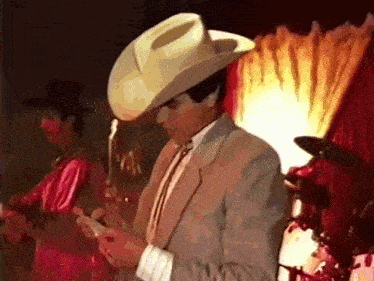 a man wearing a cowboy hat and a suit looks at his phone