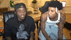 two men are sitting in chairs in a living room and looking at each other .