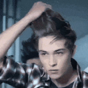 a young man in a plaid shirt is holding his hair in front of a mirror .