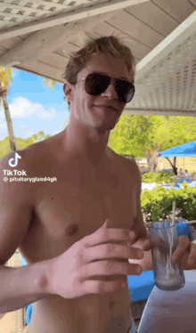 a shirtless man wearing sunglasses is holding a glass in his hand .