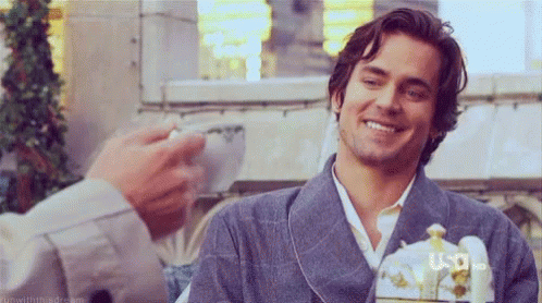 a man in a robe is smiling and holding a cup of coffee while another man looks on .