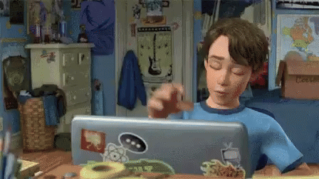 a boy is sitting at a desk using a laptop computer with stickers on it