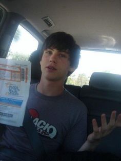 This may contain: a young man sitting in the back seat of a car holding up his hand sign