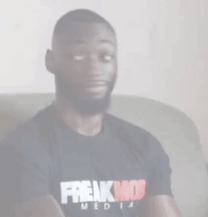 a man wearing a black t-shirt that says freakmob media is sitting on a couch .