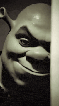 a shrek statue is peeking out from behind a wall and smiling .