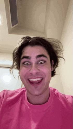 a young man wearing a pink shirt makes a funny face