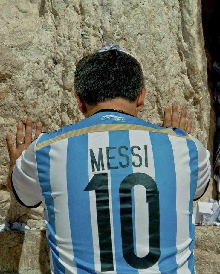 This may contain: a man wearing a blue and white jersey with the number 10 on it sitting in front of a stone wall