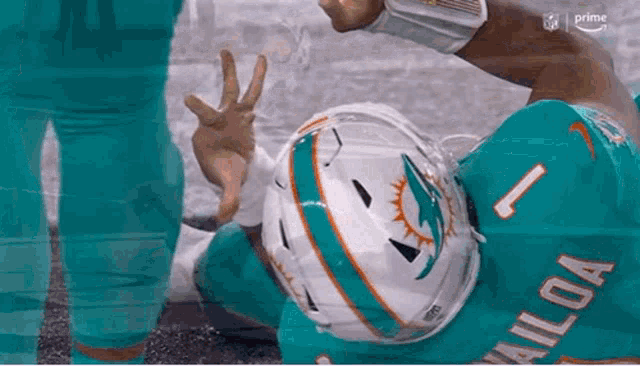 a miami dolphins football player is laying on the ground giving the peace sign .
