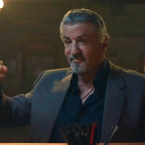 a man in a suit holds a glass of whiskey in his hand