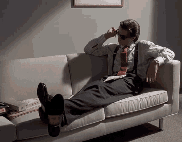 a man in a suit and tie is sitting on a couch reading a book