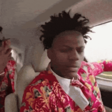 a man with dreadlocks is sitting in the back seat of a car wearing a red jacket and tie .