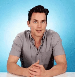 a man is sitting at a table with his hands folded in front of a blue background .
