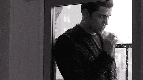 a black and white photo of a man looking out of a window .