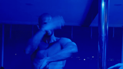 a shirtless man is standing on a pole in the dark
