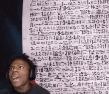 a man wearing headphones stands in front of a wall with ancient writing