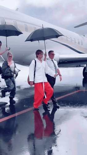 a woman in red pants carrying an umbrella walks towards a plane