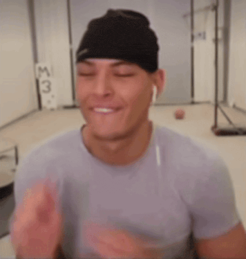 a man wearing a black beanie and ear buds is smiling with his eyes closed .