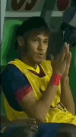 a soccer player wearing a yellow jersey is sitting with his hands folded
