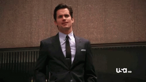 a man in a suit and tie is standing in front of a wall and smiling .