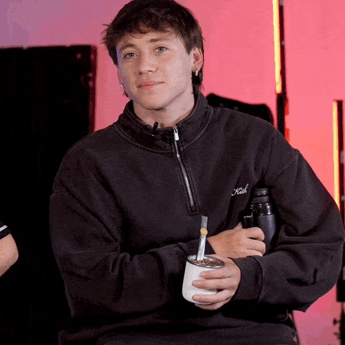 a young man in a black sweatshirt holds a cup with a straw in it