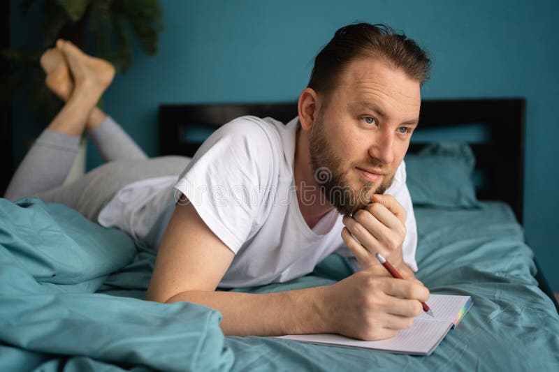 millennial-man-laying-bed-writing-diary-smiling-thoughtful-guy-notebook-pen-her-hands-millennial-man-laying-282287785.jpg